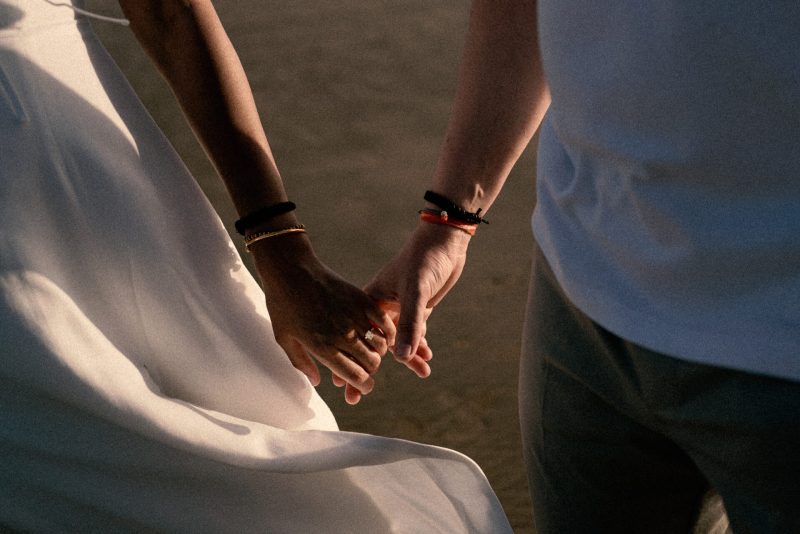 Two people holding hands, one wearing a white dress and the other in casual attire, symbolize companionship in front of a FREE photobooth.