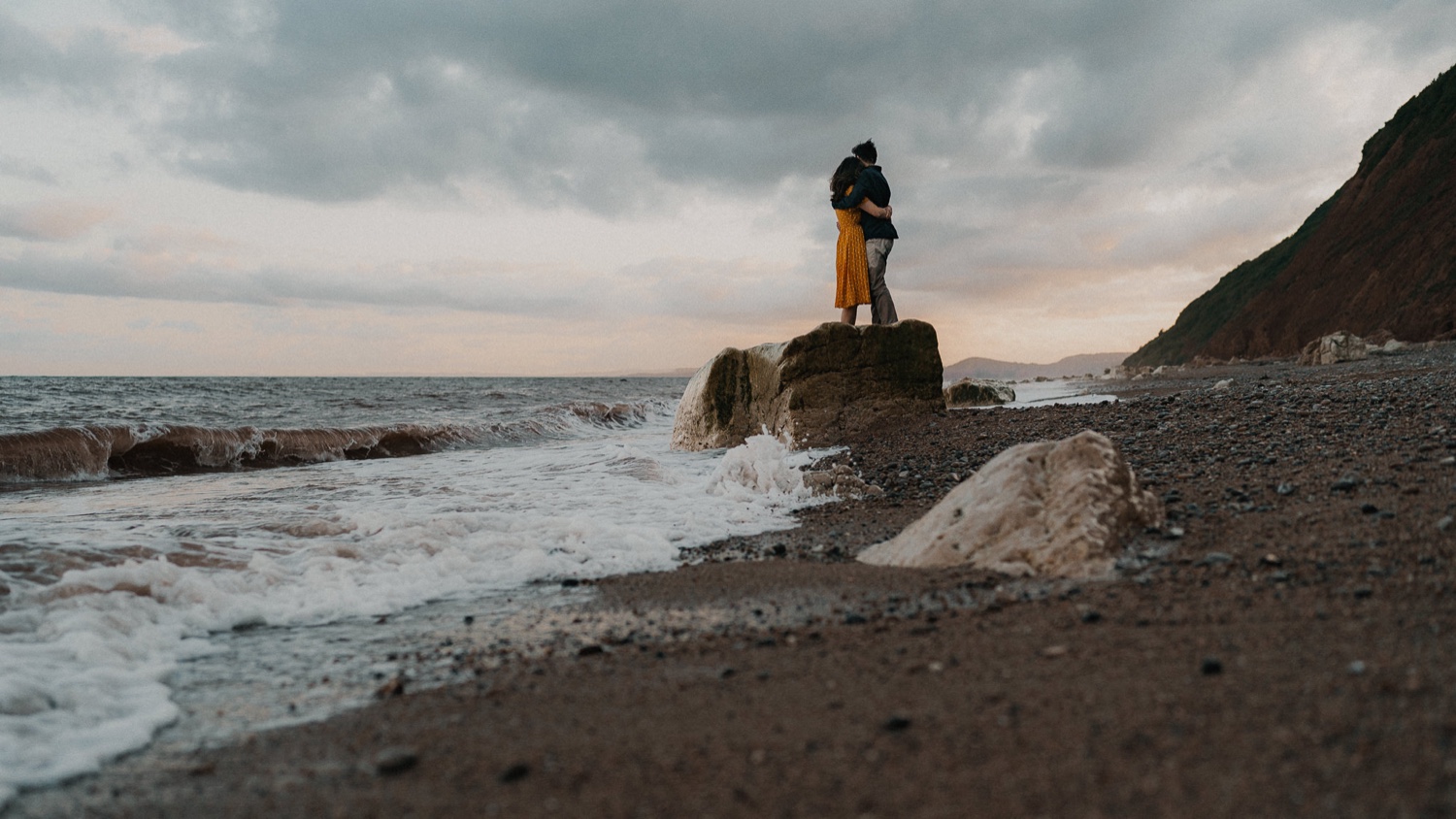 Wedding couple posing on beach rocks at sunset.